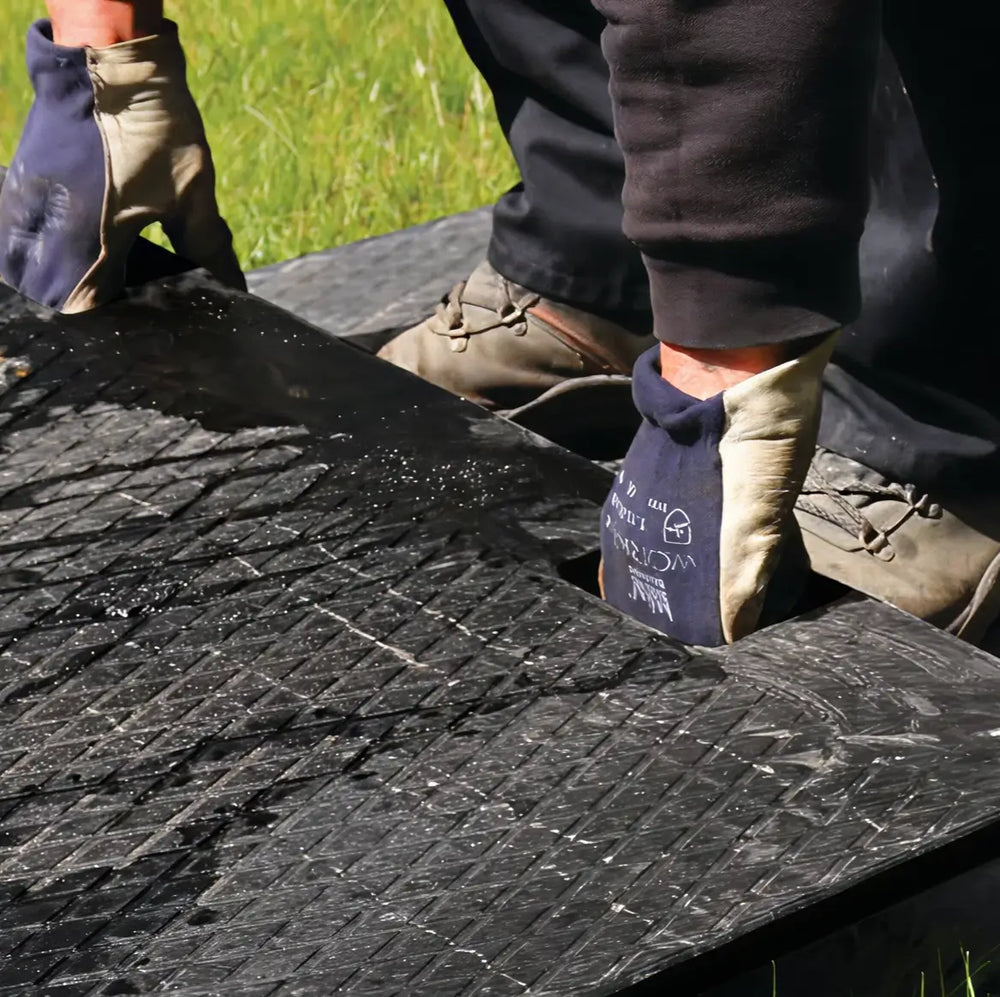 Close-up of a worker wearing gloves connecting two interlocking black ground protection mats on grass