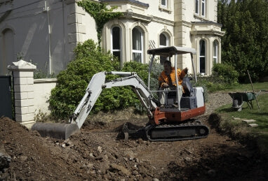 Construction worker operating a mini excavator on residential property, illustrating the need for grass protection mats to safeguard the lawn.