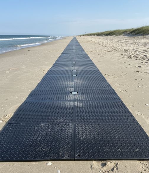 Black modular beach access mat pathway extending across a sandy beach toward the ocean.