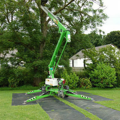 Ground protective mats under a large green machine at a treeline.