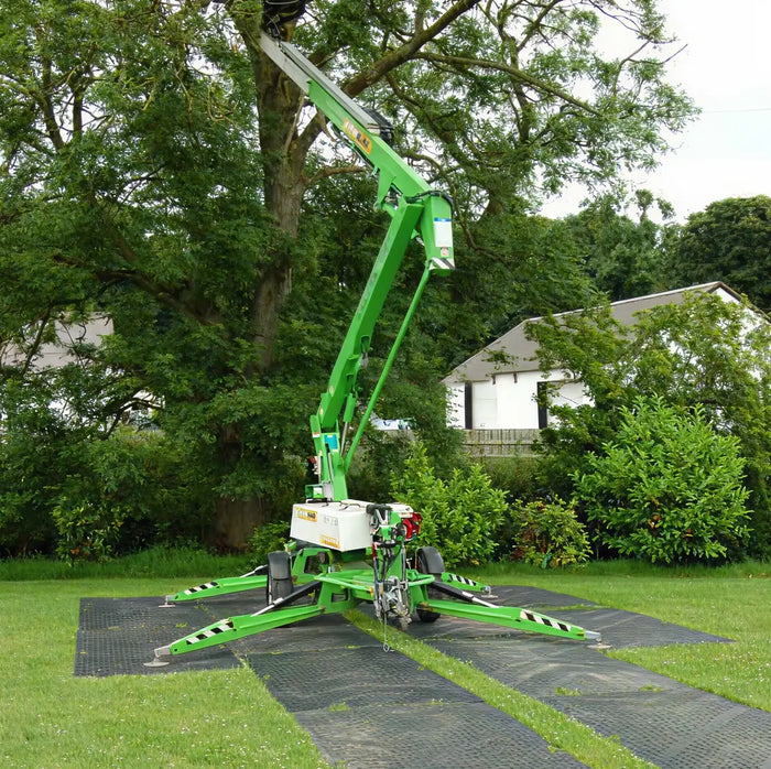 Ground protective mats under a large green machine at a treeline.