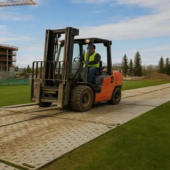 Forklift driving over durable ground protection mats on grass.