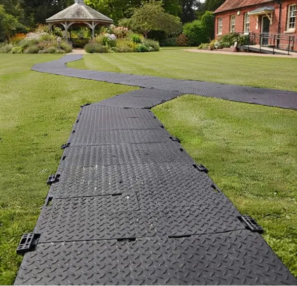 Black interlocking portable walkway mats laid across a grass lawn leading to a garden gazebo.