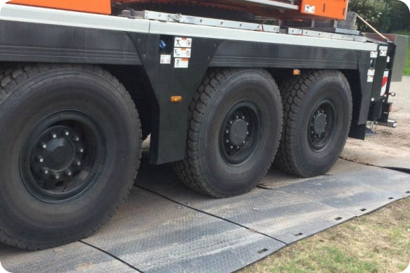 Heavy truck wheels on weight distribution mats protecting grass surface.
