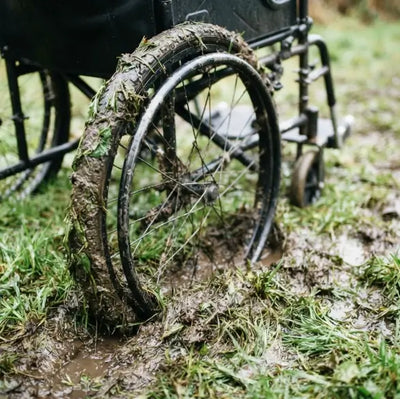 Close-up of a wheelchair's wheels caked in mud after crossing wet, uneven grass.